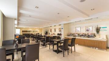 A modern hotel dining area with multiple tables and chairs, a reception desk, and a clean, well-lit interior.