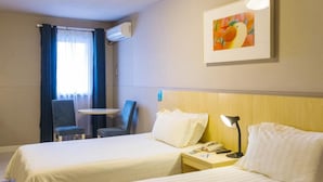 A hotel room with two beds, a desk, a chair, a lamp, and a painting on the wall. - Jinjiang Inn (Daqing)