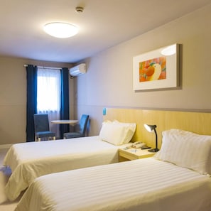Habitación de hotel con dos camas, un escritorio, una silla, una lámpara y un cuadro en la pared.