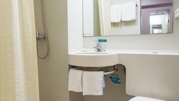A bathroom with a shower, sink, mirror, and toilet.