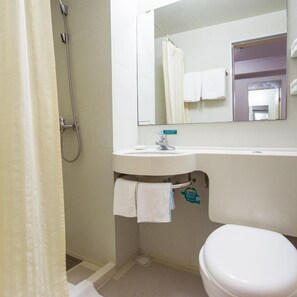Un baño con ducha, lavamanos, espejo e inodoro.