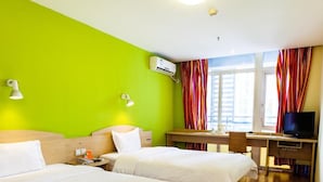 Ein Hotelzimmer mit zwei Betten, einem Schreibtisch mit Fernseher und einem Fenster mit Vorhängen.