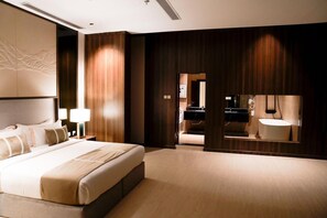 Una habitación de hotel moderna con una cama grande, una mesita de noche, un televisor montado en la pared y un baño visible a través de una puerta abierta.
