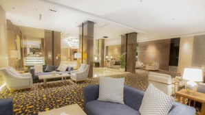 Un vestíbulo amplio con un sofá azul, sillones y una mesa de centro.
