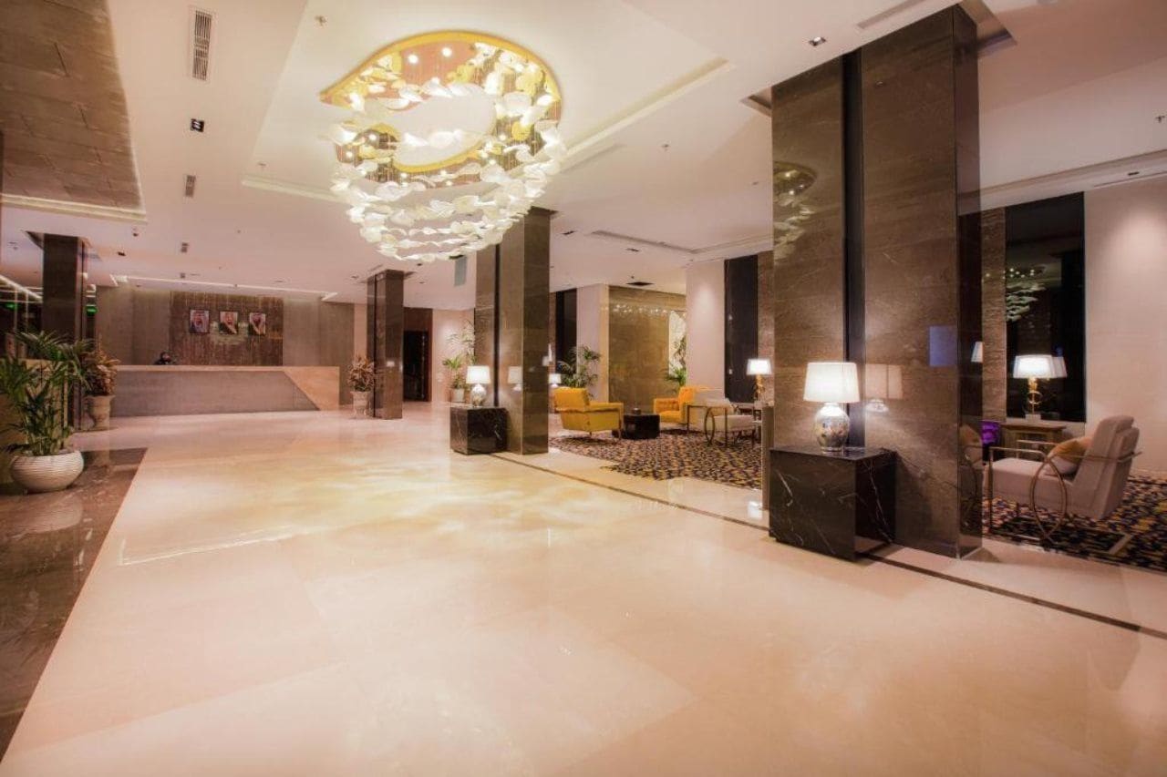 A spacious lobby with a marble floor, a large chandelier, and seating areas with lamps.