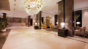 A spacious lobby with a marble floor, a large chandelier, and seating areas with lamps.