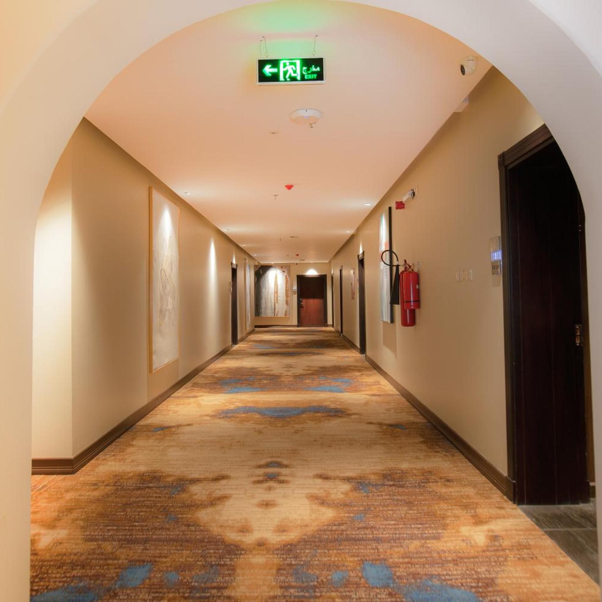 A hotel corridor with an exit sign, a fire extinguisher, and a door at the end.