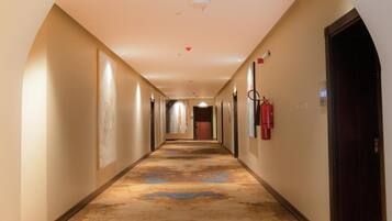 A hotel corridor with an exit sign, a fire extinguisher, and a door at the end.