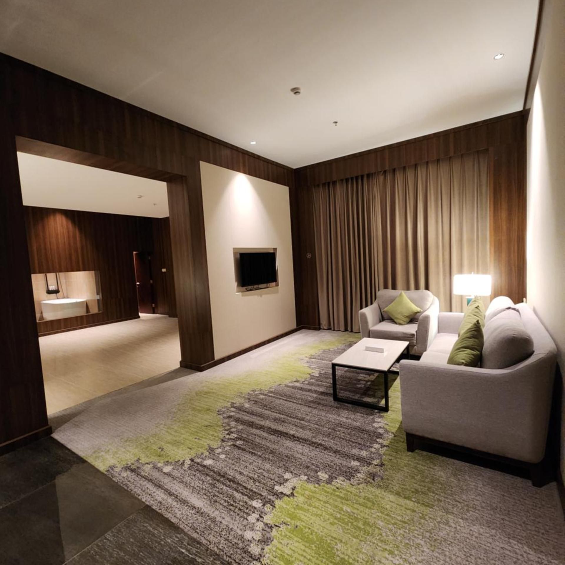 A modern living room with a sofa, a coffee table, and a television. There is a hallway leading to a bathroom.