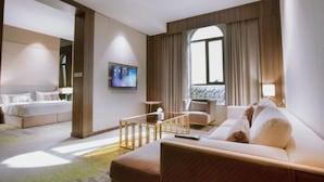 Habitación de hotel con cama, sofá, televisor y ventana con cortinas.