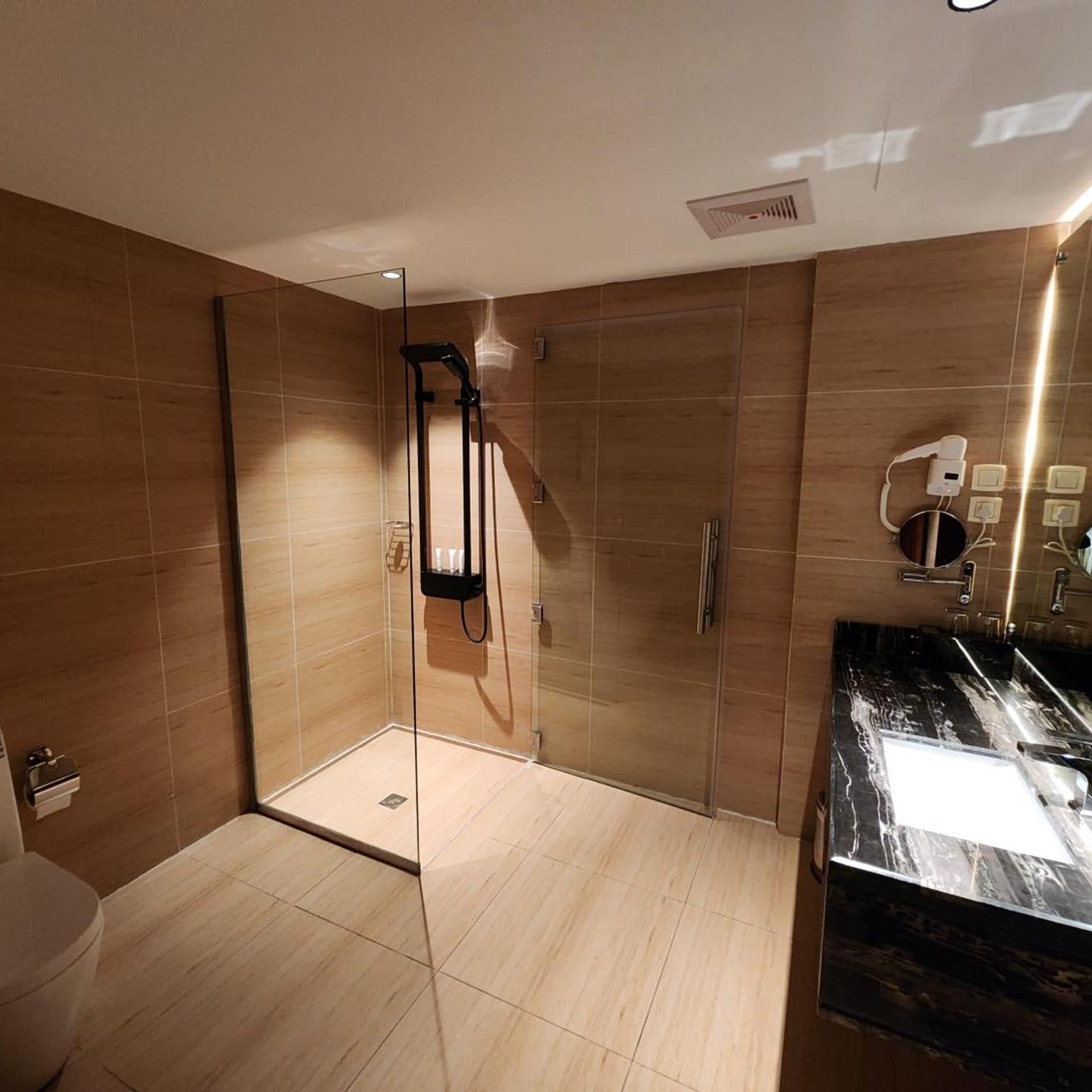 Un baño moderno con ducha envuelta en vidrio, encimera de mármol y un secador de pelo de pared.