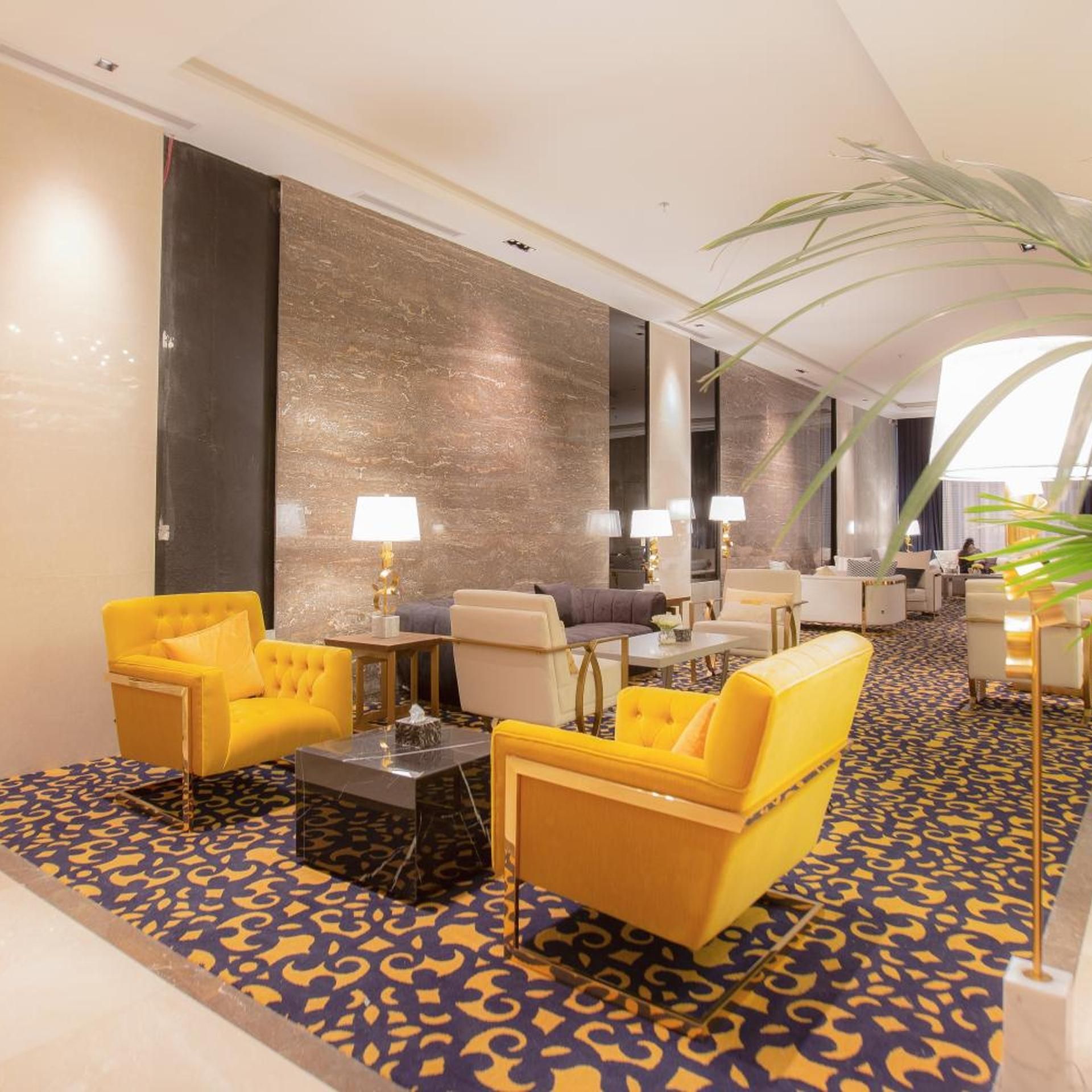 A hotel lobby with a patterned carpet, yellow armchairs, a sofa, and a coffee table.