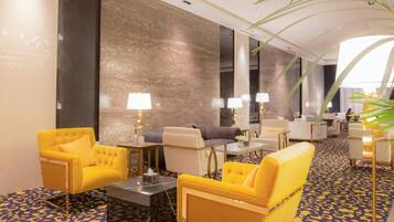 A hotel lobby with a patterned carpet, yellow armchairs, a sofa, and a coffee table.