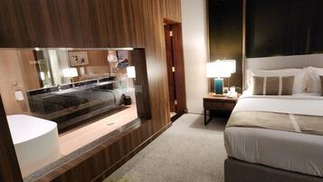 A hotel room with a large bed, a bedside table with a lamp, a mirror, and a view of the outside.