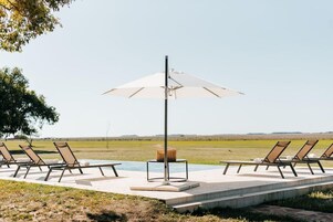 Zona junto a la piscina con sillas de descanso y una sombrilla grande.