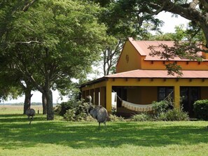 A yellow building with a red roof, surrounded by trees and grass.