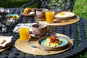Una mesa al aire libre con desayuno servido, platos de comida, vasos de jugo de naranja y una taza.
