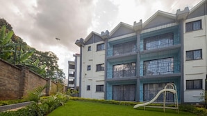 A multi-story residential building with a white facade, balconies, and a playground area. - Sports Road Apartments (Nairobi)