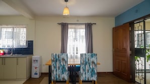 A dining area with a table and chairs, a water dispenser, and a door leading outside. - Sports Road Apartments (Nairobi)
