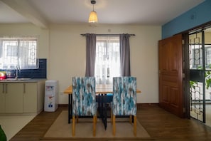 Een eetruimte met een tafel, stoelen, een waterdispenser en een deur naar buiten.