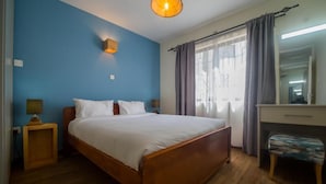 A bedroom with a wooden bed, a nightstand, a desk, and a chair. - Sports Road Apartments (Nairobi)