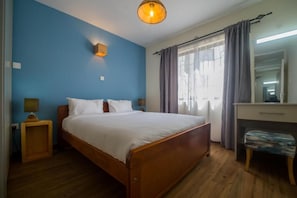 Een slaapkamer met een houten bed, nachtkastje, bureau en stoel.