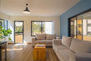 Una sala de estar moderna con un sofá, una mesa de centro y ventanas amplias.