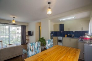 Una cocina moderna con armarios blancos, una mesa de comedor de madera y un ventanal con cortinas.