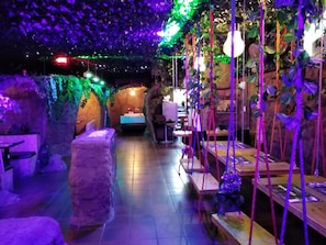 Un espace intérieur à l’ambiance rustique, comprenant un mur en pierre, des bancs en bois et des plantes suspendues.