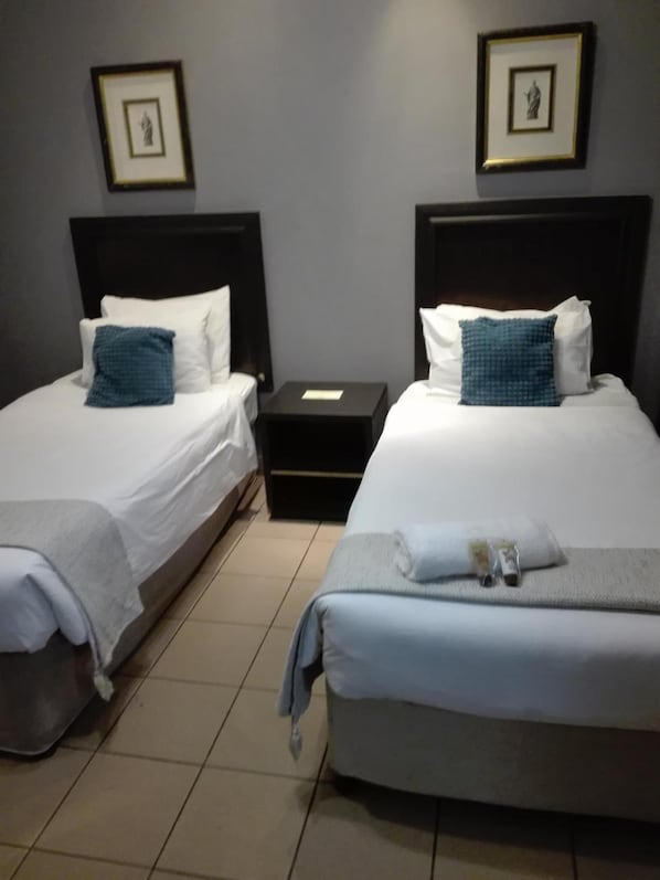 Une chambre d’hôtel avec deux lits, chacun agrémenté de draps blancs et d’oreillers bleus, une petite table de chevet et des tableaux encadrés accrochés au mur.