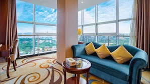 Habitación de hotel moderna con un ventanal grande, un sofá con cojines, una pequeña mesa redonda y una silla.