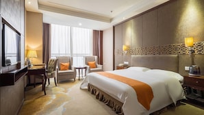Una habitación de hotel con una cama grande, dos sillones, un escritorio con lámpara y un televisor.