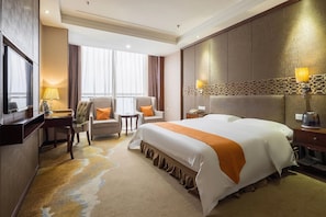 Een hotelkamer met een groot bed, twee fauteuils, een bureau met een lamp en een televisie.