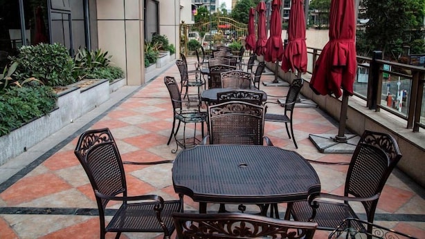 Un área de estar al aire libre con mesas y sillas, rodeada de edificios y follaje.