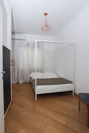 Ein Zimmer mit einem Himmelbett, Holzboden, einer weißen Tür und einer Deckenleuchte.