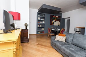 Ein modernes Wohnzimmer mit einem grauen Sofa, einem Holzschrank und einem Fernseher auf einem gelben Podest.