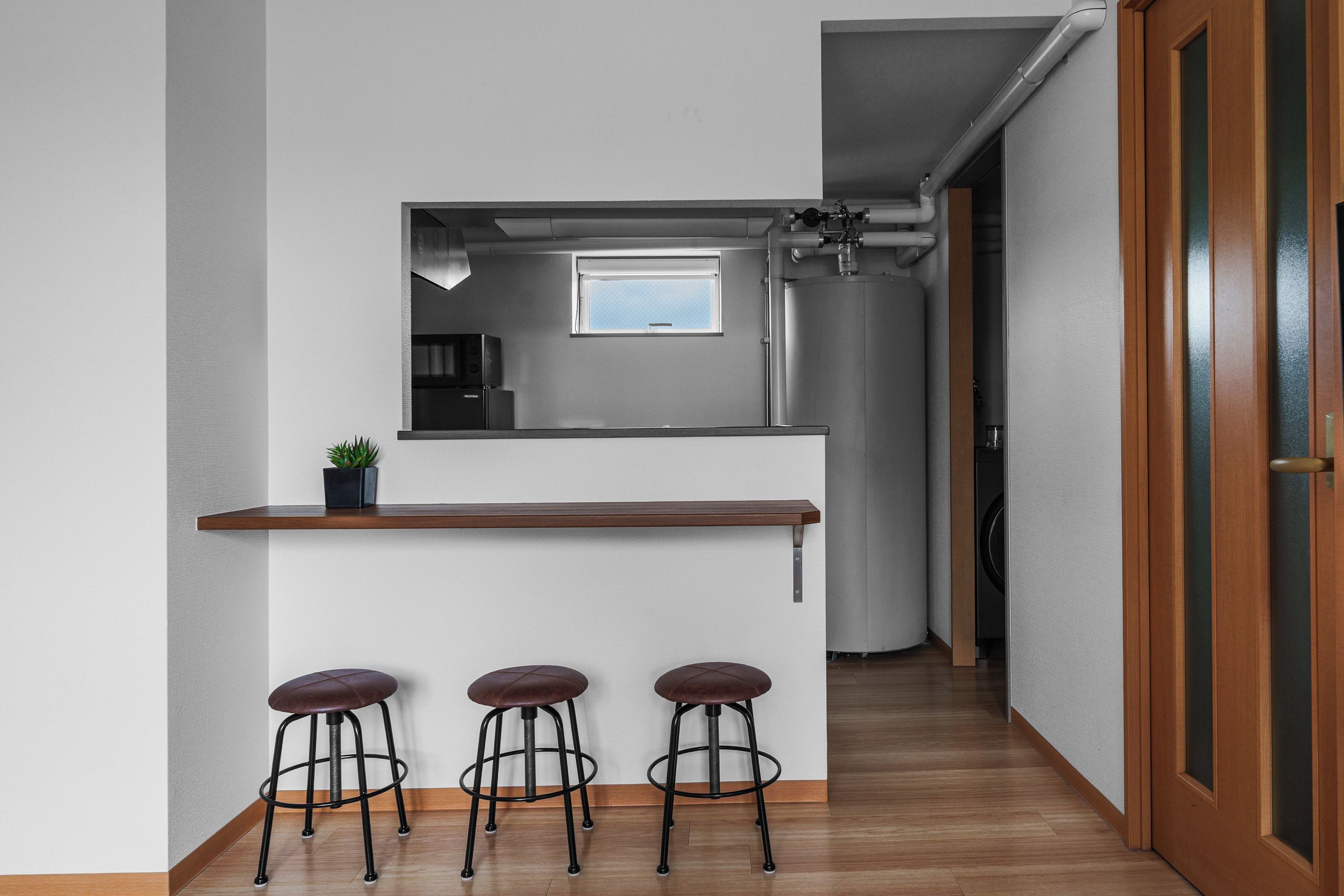 A compact kitchen with a built-in microwave, a small window, and a wooden counter with stools.