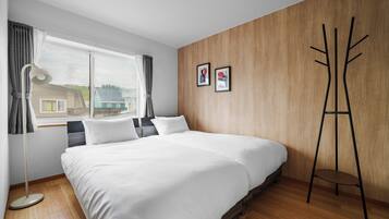 A bedroom with a large bed, a standing lamp, a window with curtains, and two framed pictures on the wall.
