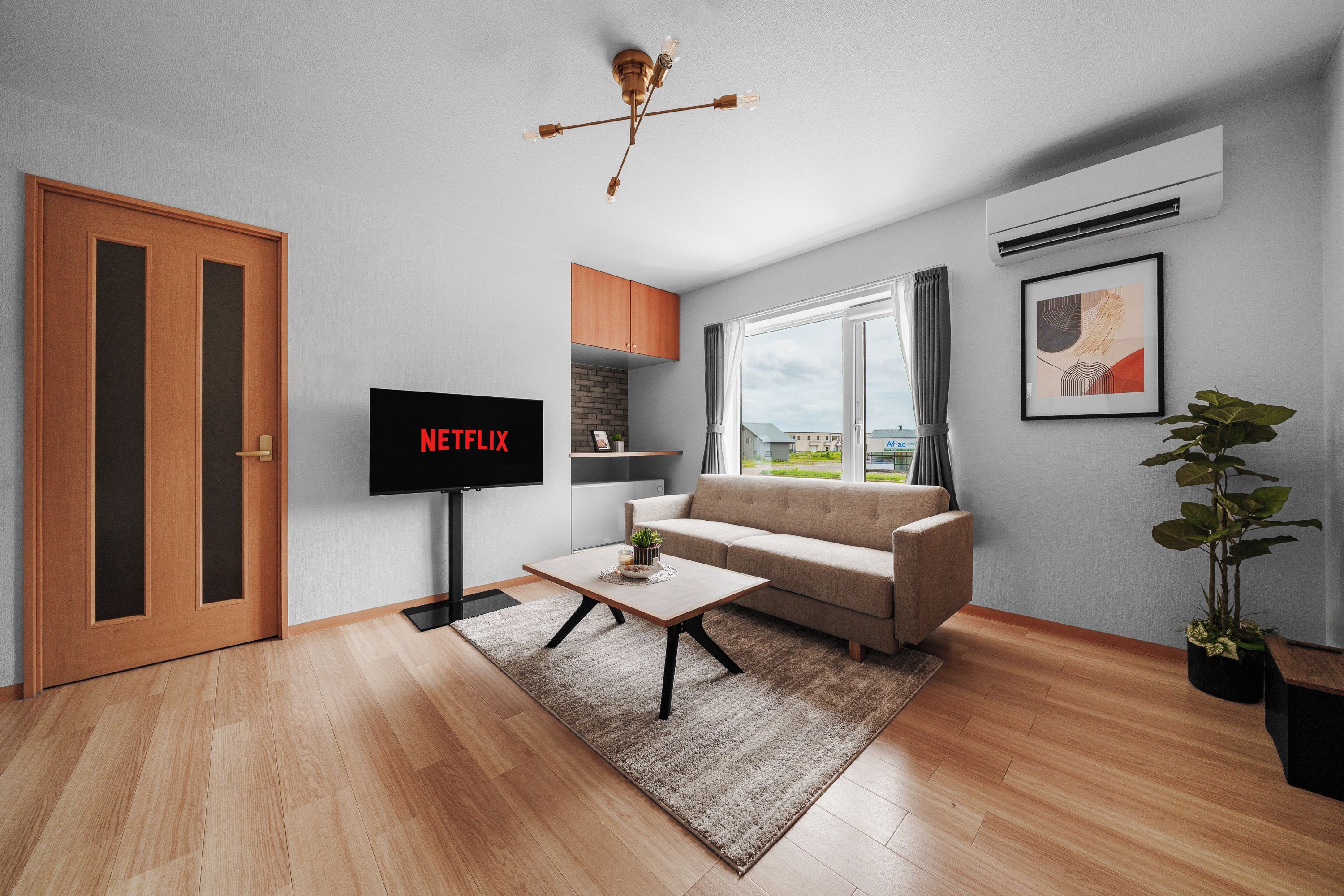 A modern living room with a flat-screen TV, a sofa, a coffee table, and a view of the outside.