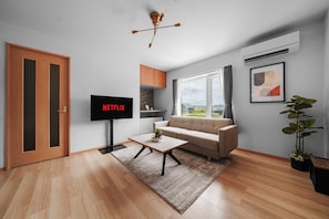 A modern living room with a flat-screen TV, a sofa, a coffee table, and a view of the outside.
