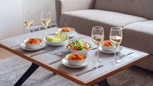A dining table with various dishes and glasses of white wine, set on a carpeted floor with a sofa in the background. - SHINTO NEST 202 (Asahikawa)