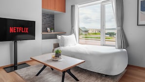 A modern hotel room with a bed, a TV mounted on the wall, a small table with a plant, and a window with curtains. - SHINTO NEST 202 (Asahikawa)