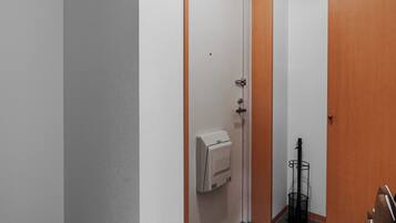 A hallway with a door, a hand dryer, and a rack with items.