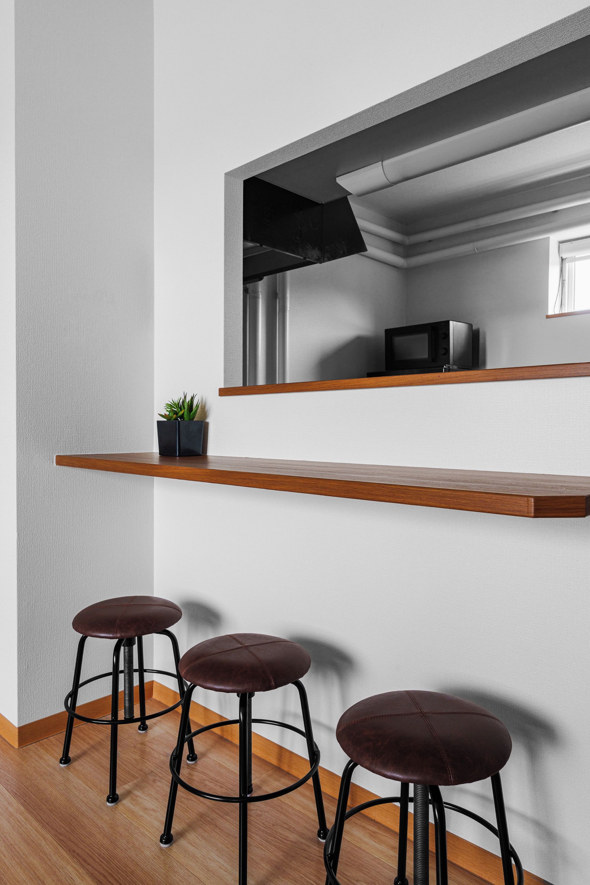 A modern kitchen with a built-in microwave, a wooden shelf, and three bar stools.