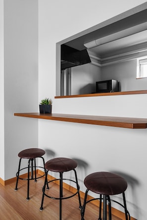 A modern kitchen with a built-in microwave, a wooden shelf, and three bar stools.