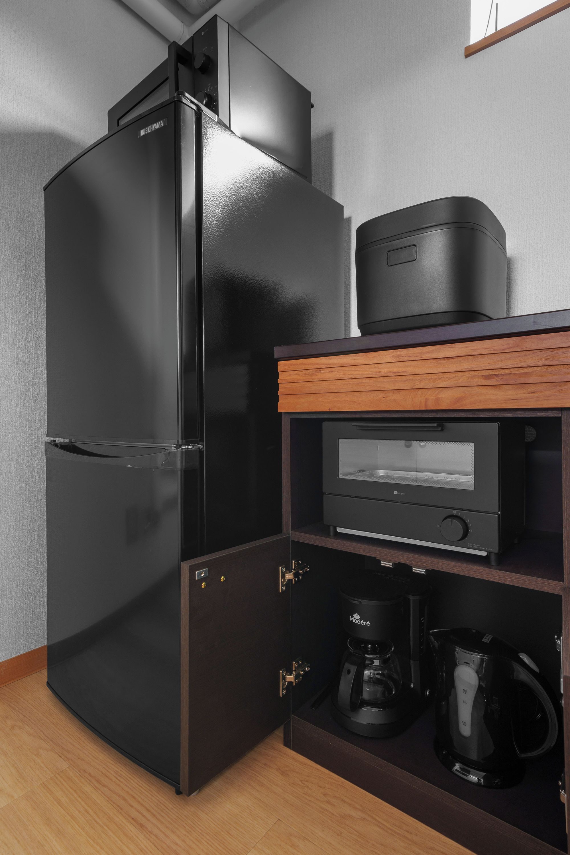 Cocina compacta con refrigerador negro, cafetera y microondas sobre una repisa de madera.