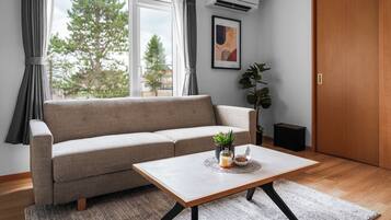 A modern living room with a sofa, a coffee table with decorative items, a potted plant, and a door.