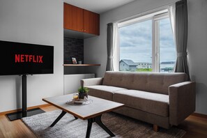 Una sala de estar moderna con un sofá, una mesa de centro, un televisor y una ventana con cortinas.