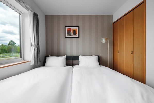 A double bed with white linens, a framed abstract painting above it, a bedside lamp, and a wooden wardrobe.