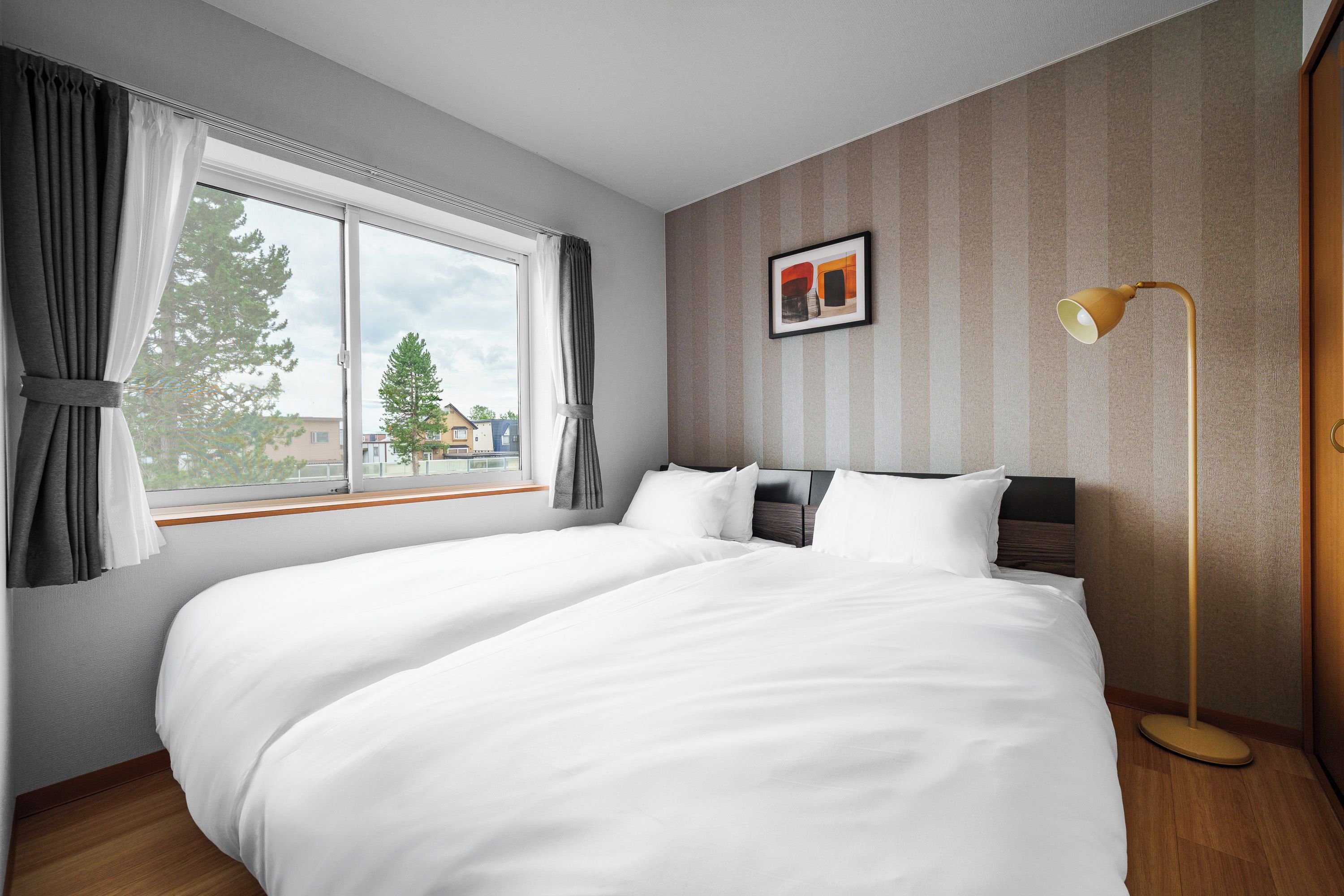 Una habitación de hotel con una cama grande, una mesita de noche, una lámpara y un ventanal con cortinas.